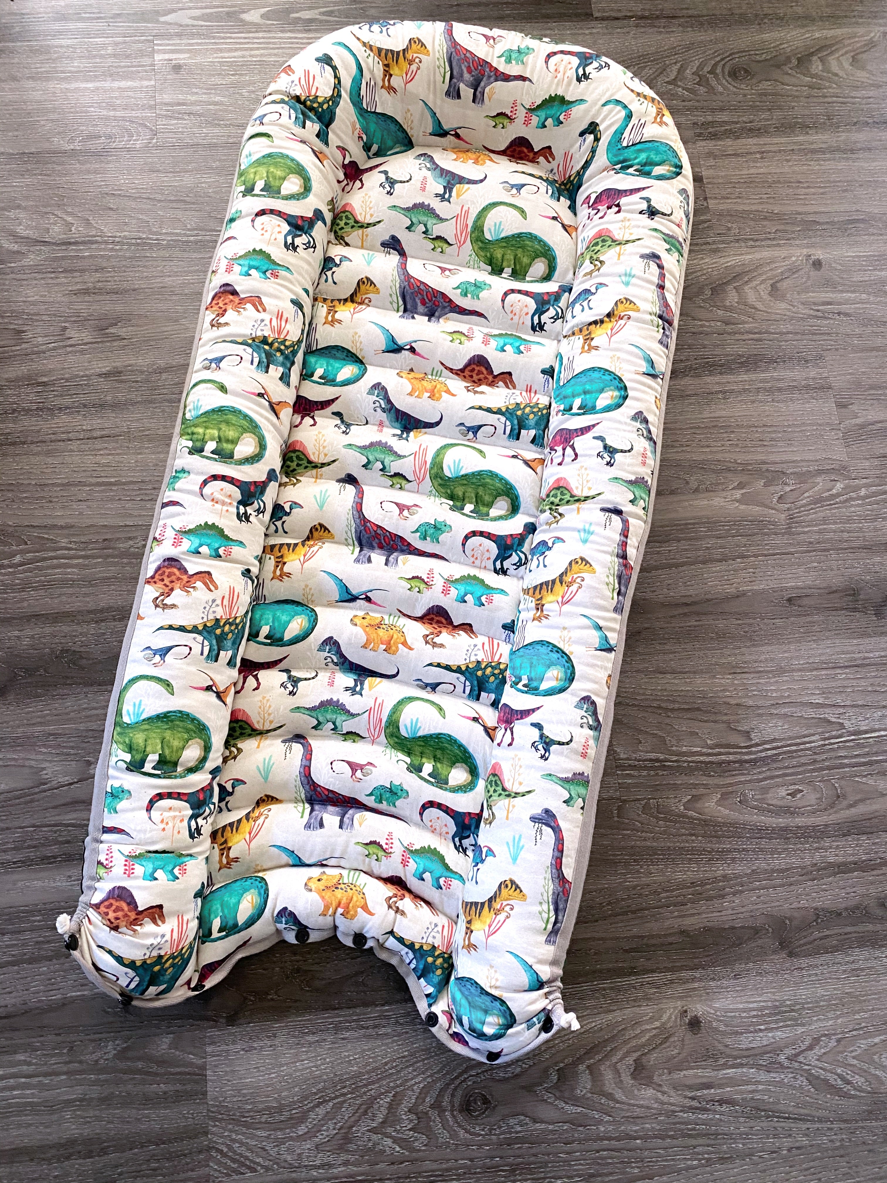 baby nest , baby lounging nest, co-sleeper, similar to dockatot and snuggle me products. This one is featured in a bright dino and green design.